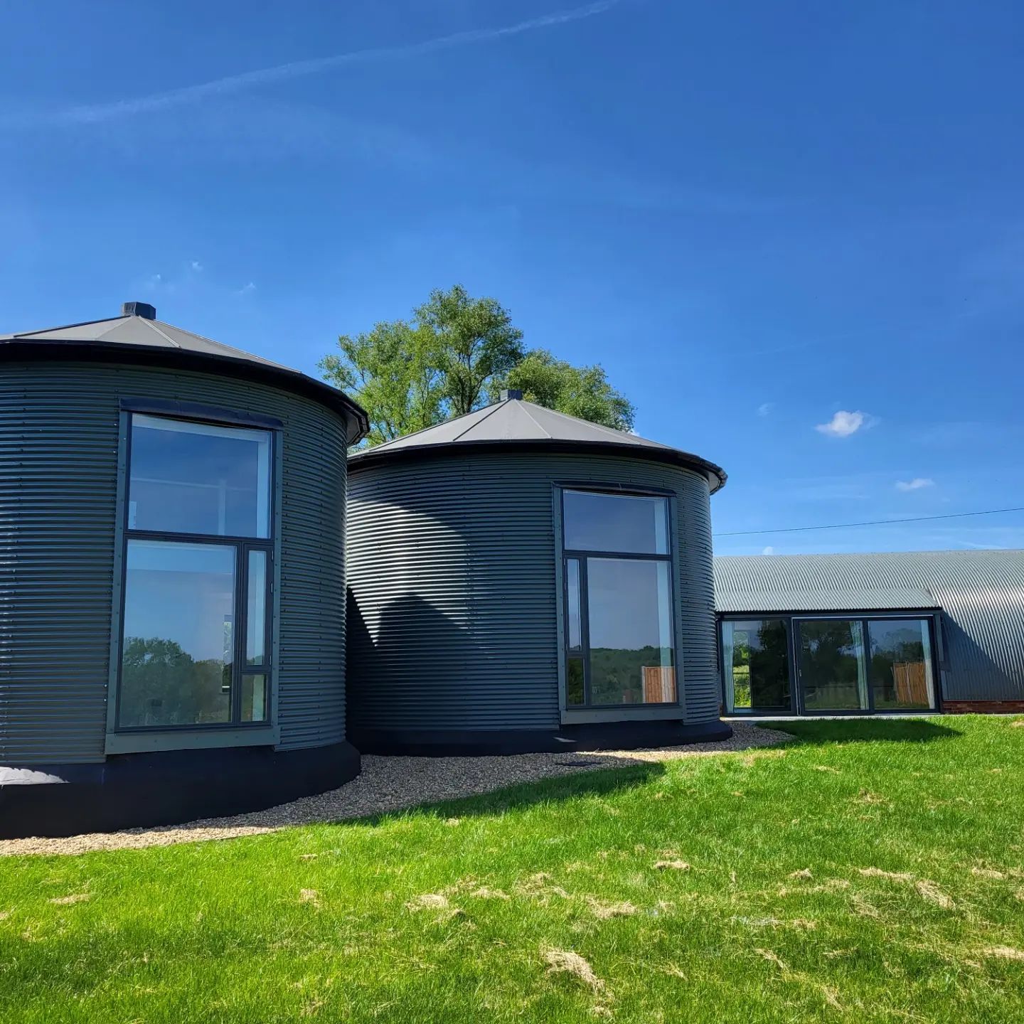 Two round corrugated buildings painted dark grey with large windows
