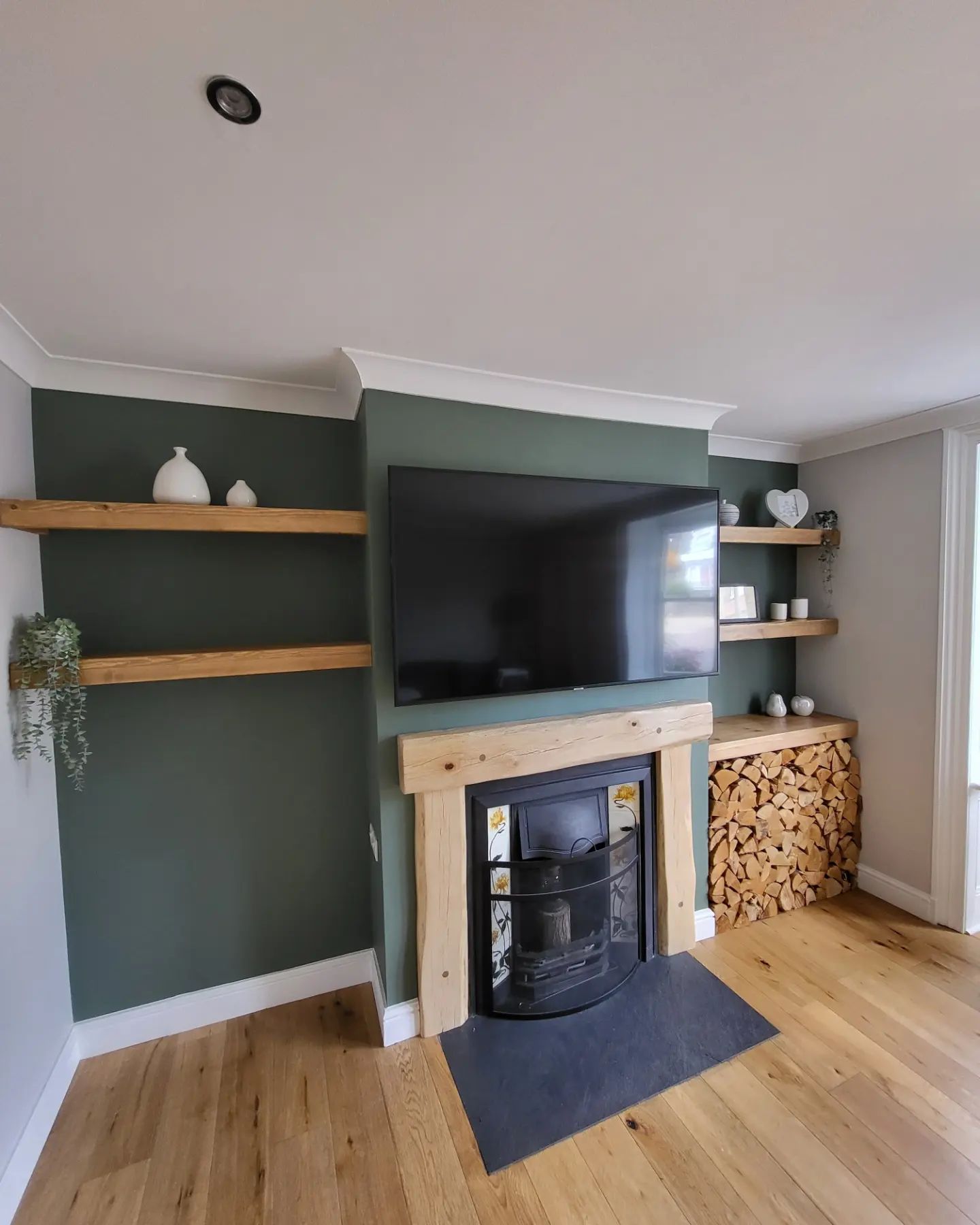 Living room with a sage green chimney breast, oak shelves and a log burner