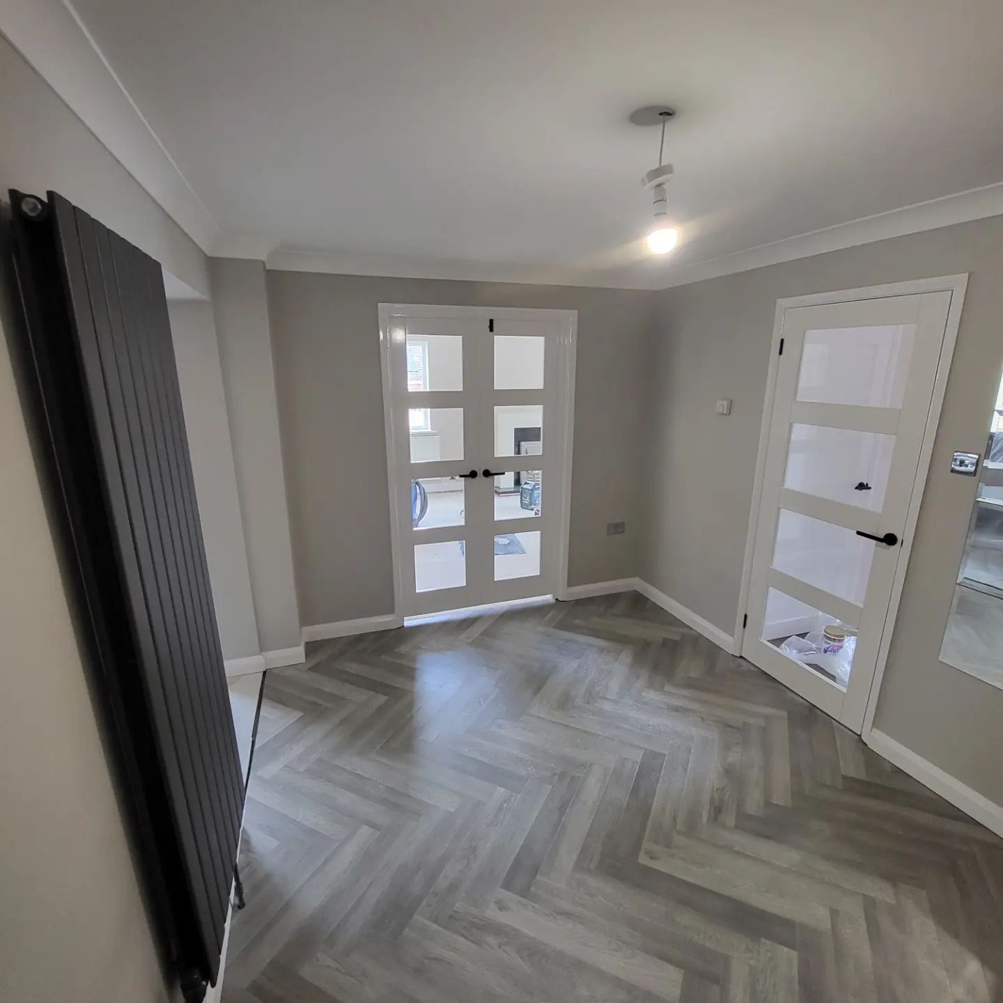 Grey room with white glazed doors, herringbone floor and a black column radiator